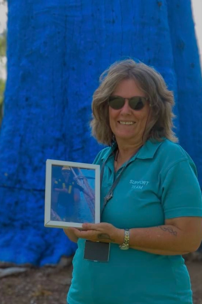 Debbie Schulze standing in front of the Big Blue Tree, holding a photo of her son James